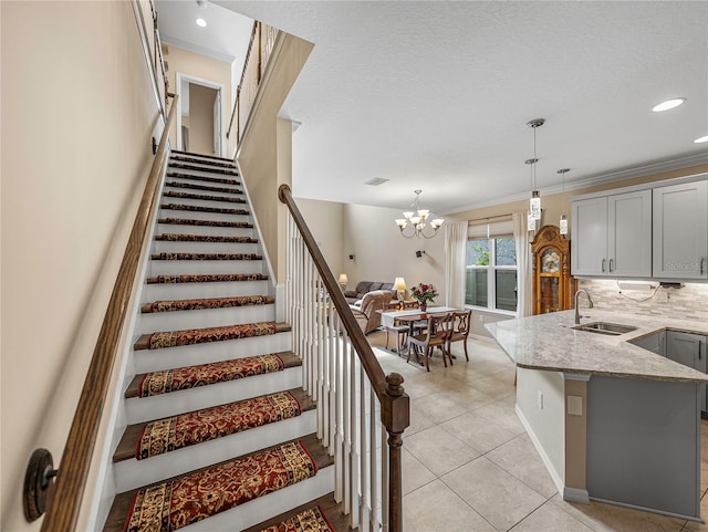 stairway with sink, an inviting chandelier, tile patterned floors, crown molding, and a textured ceiling