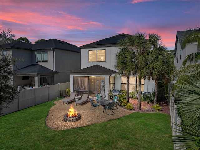 back house at dusk featuring a lawn and an outdoor fire pit