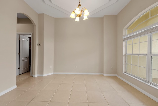 unfurnished room with light tile patterned floors, a tray ceiling, and a chandelier