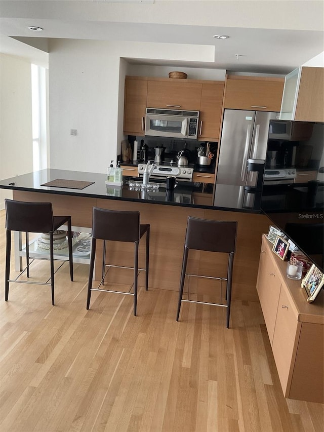 kitchen featuring a breakfast bar, stainless steel appliances, kitchen peninsula, and light hardwood / wood-style floors