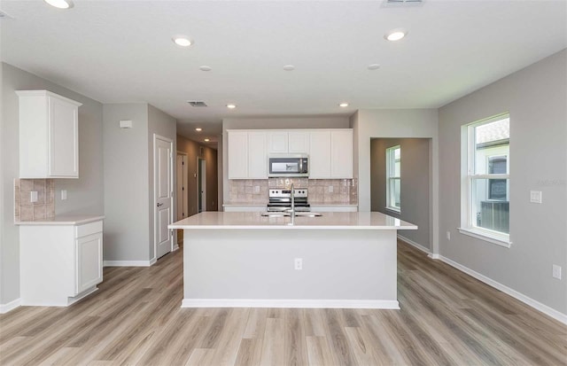 kitchen with an island with sink, light hardwood / wood-style flooring, white cabinets, and stainless steel appliances