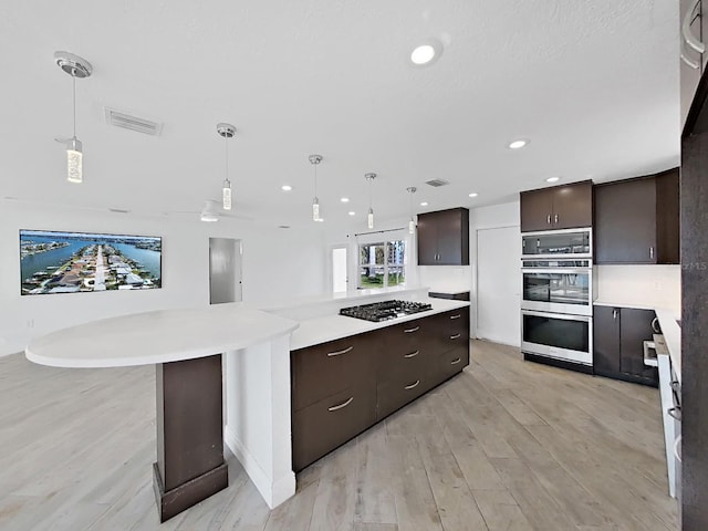 kitchen featuring pendant lighting, gas stovetop, a kitchen island, dark brown cabinets, and light hardwood / wood-style floors