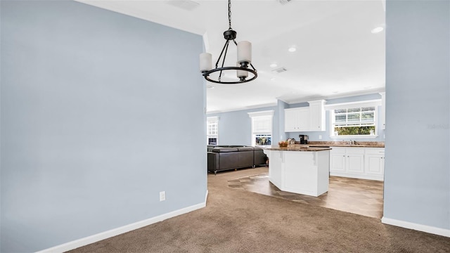 kitchen with light carpet, an inviting chandelier, dark stone countertops, white cabinets, and a center island