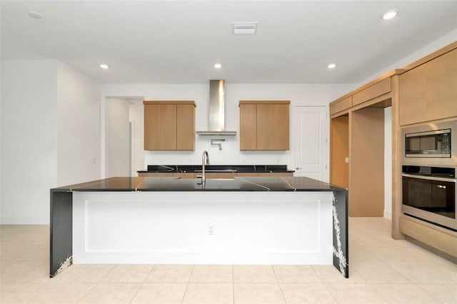 kitchen with sink, stainless steel appliances, wall chimney range hood, an island with sink, and light tile patterned flooring