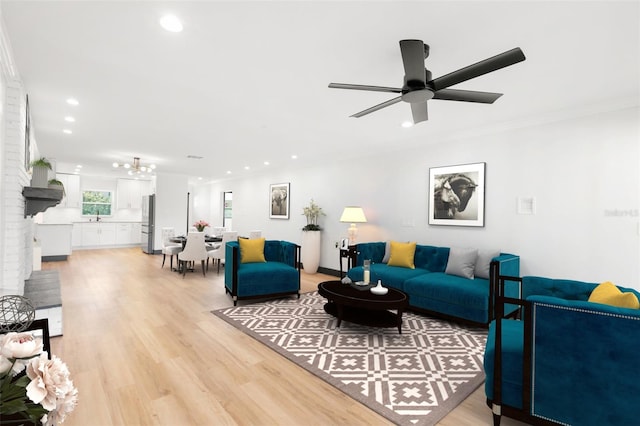 living room with light wood-type flooring, a brick fireplace, ceiling fan, crown molding, and sink