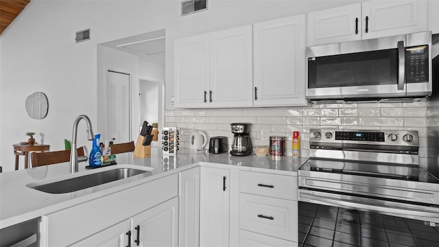 kitchen featuring appliances with stainless steel finishes, tasteful backsplash, light stone counters, sink, and white cabinetry