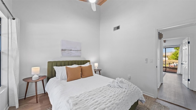 bedroom with access to exterior, ceiling fan, hardwood / wood-style floors, and a high ceiling