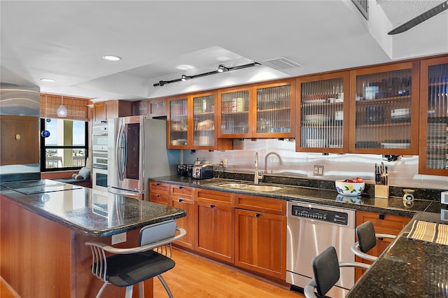 kitchen with sink, light hardwood / wood-style flooring, appliances with stainless steel finishes, dark stone countertops, and a kitchen bar