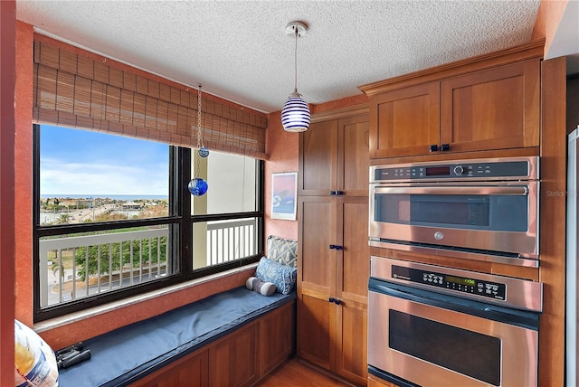 kitchen featuring double oven, hanging light fixtures, light hardwood / wood-style floors, and a textured ceiling