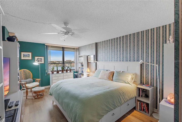 bedroom featuring a water view, ceiling fan, light hardwood / wood-style floors, and a textured ceiling