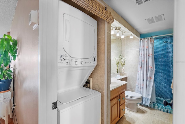 bathroom with tile patterned floors, toilet, tile walls, vanity, and stacked washer / dryer