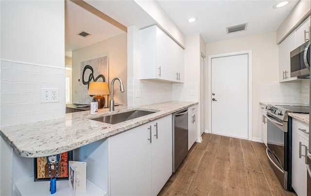 kitchen featuring kitchen peninsula, appliances with stainless steel finishes, light stone counters, sink, and white cabinets