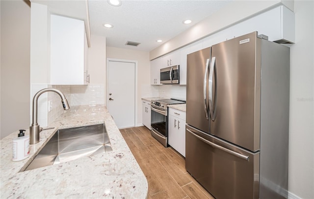 kitchen featuring appliances with stainless steel finishes, light stone counters, white cabinetry, and sink