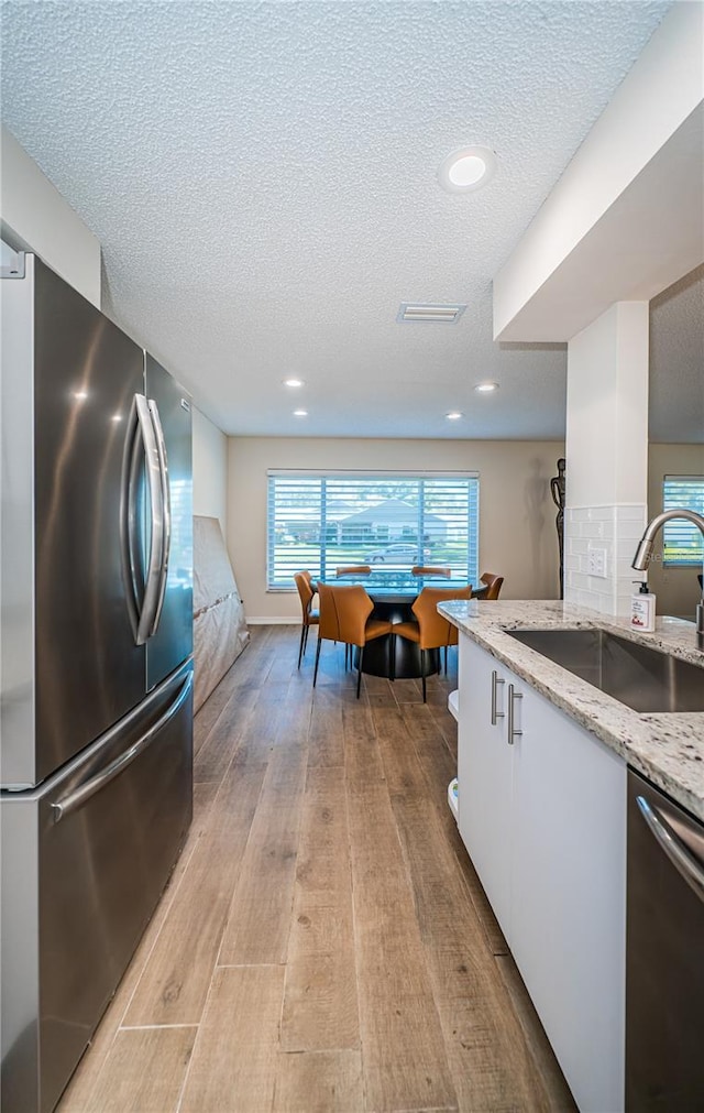 kitchen with decorative backsplash, light stone counters, stainless steel appliances, sink, and white cabinets