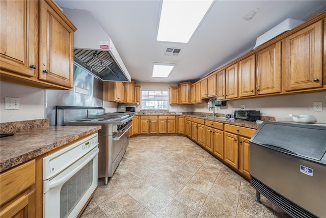 kitchen with a skylight, white oven, high end stainless steel range oven, sink, and wall chimney range hood