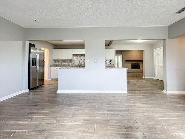 kitchen featuring kitchen peninsula, stainless steel fridge, tasteful backsplash, a textured ceiling, and white cabinets