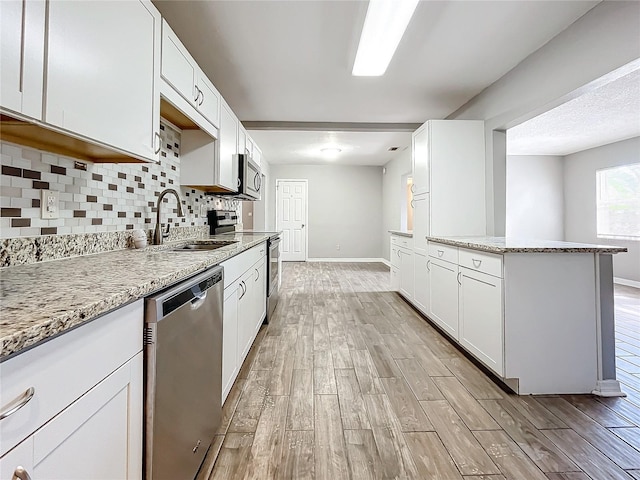 kitchen with white cabinets, sink, light wood-type flooring, appliances with stainless steel finishes, and light stone counters