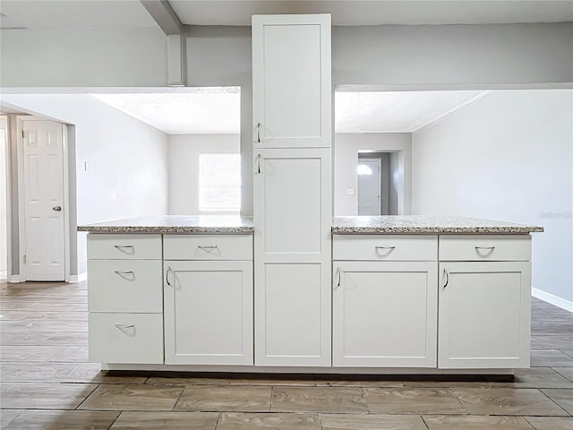 kitchen featuring kitchen peninsula, light stone countertops, white cabinets, and light wood-type flooring