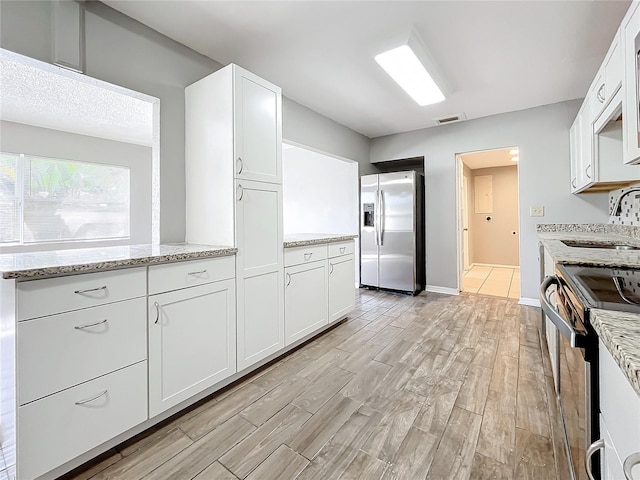 kitchen with light stone countertops, sink, light hardwood / wood-style floors, white cabinets, and appliances with stainless steel finishes