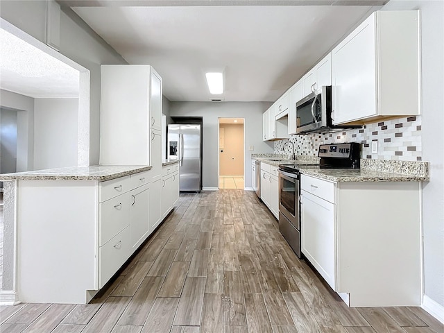 kitchen featuring wood-type flooring, white cabinetry, kitchen peninsula, and appliances with stainless steel finishes