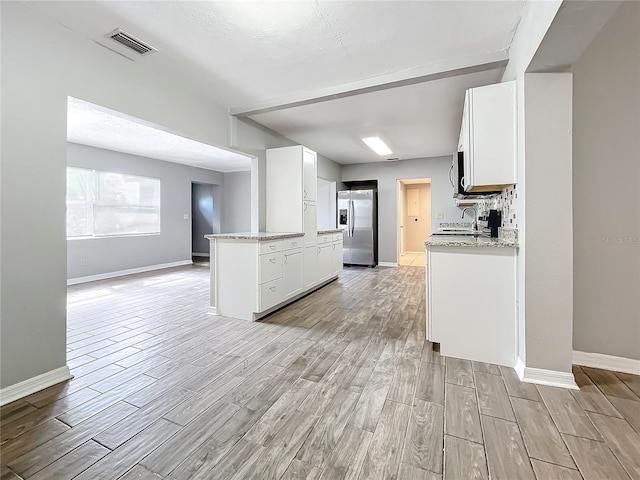 kitchen featuring white cabinets, sink, stainless steel fridge, light hardwood / wood-style floors, and light stone counters