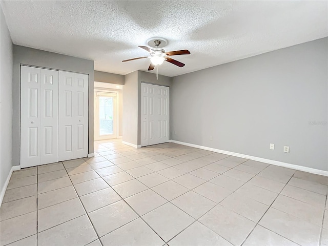 unfurnished bedroom featuring light tile patterned floors, a textured ceiling, ceiling fan, and multiple closets