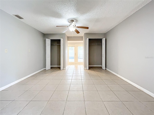 unfurnished bedroom featuring french doors, two closets, ceiling fan, light tile patterned floors, and a textured ceiling