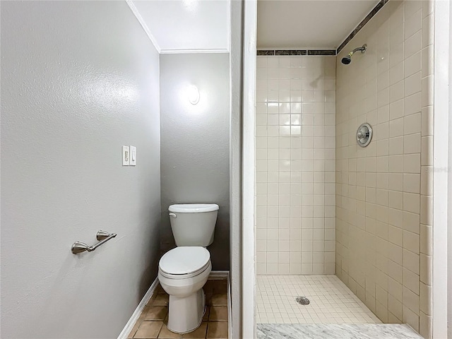 bathroom with tile patterned floors, crown molding, toilet, and tiled shower