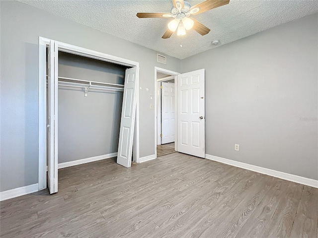 unfurnished bedroom with a textured ceiling, a closet, light hardwood / wood-style flooring, and ceiling fan