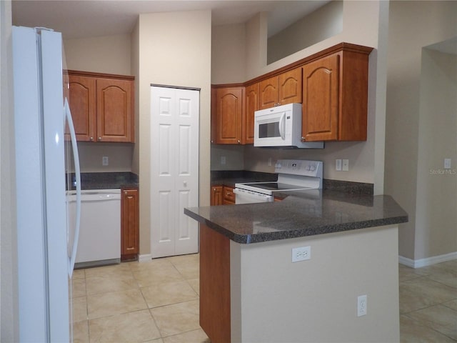 kitchen with kitchen peninsula, light tile patterned floors, dark stone counters, and white appliances