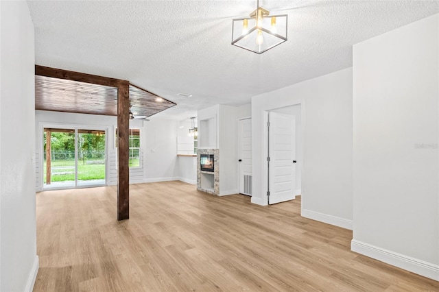 unfurnished living room with light hardwood / wood-style flooring, a textured ceiling, and a notable chandelier