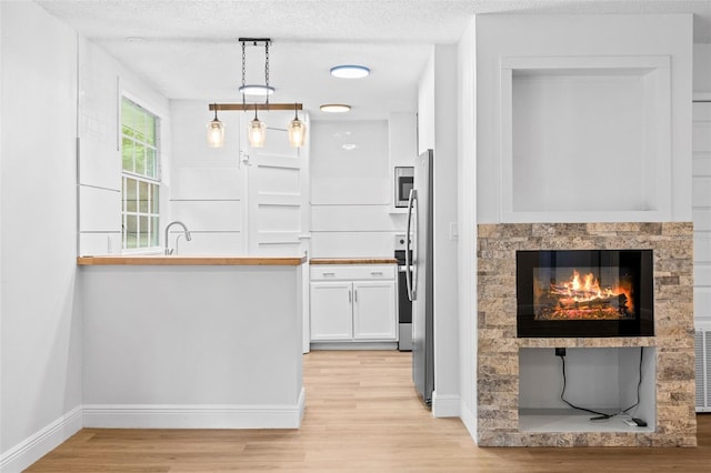 kitchen with decorative light fixtures, white cabinetry, a textured ceiling, and light hardwood / wood-style flooring