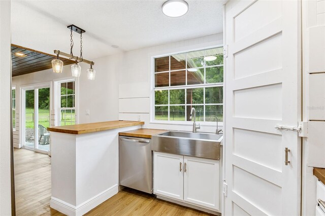 kitchen featuring stainless steel dishwasher, sink, light hardwood / wood-style flooring, white cabinets, and hanging light fixtures