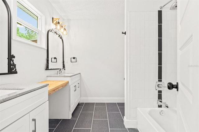 bathroom with a textured ceiling, vanity, and tiled shower / bath combo