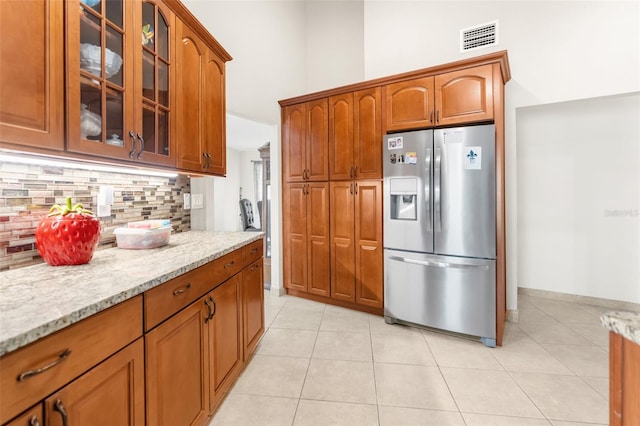 kitchen with light tile patterned flooring, light stone counters, stainless steel fridge with ice dispenser, and backsplash