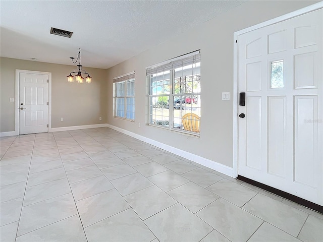 tiled entryway featuring a textured ceiling and a chandelier