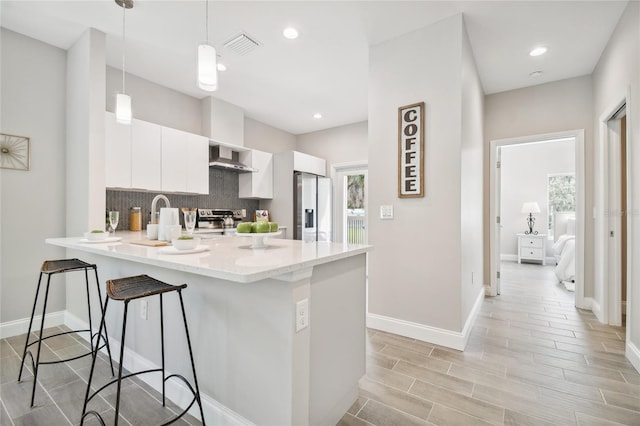 kitchen featuring pendant lighting, white cabinets, light hardwood / wood-style flooring, kitchen peninsula, and stainless steel appliances