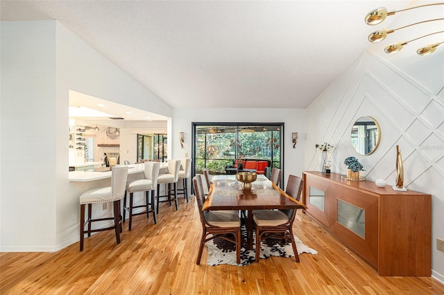 dining space featuring a textured ceiling, light wood-type flooring, and lofted ceiling