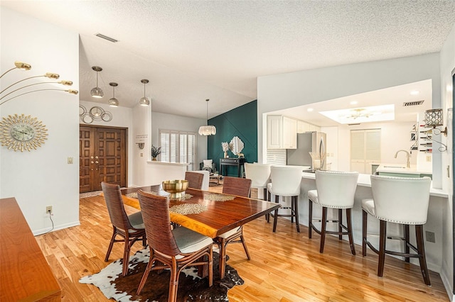 dining area with a chandelier, a textured ceiling, light wood-type flooring, and lofted ceiling