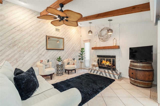 living room featuring ceiling fan, beam ceiling, light tile patterned floors, a stone fireplace, and wood walls