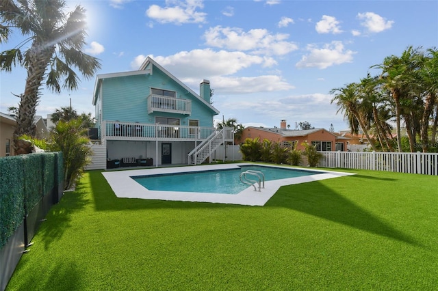 rear view of property featuring a fenced in pool, a balcony, a lawn, and a patio