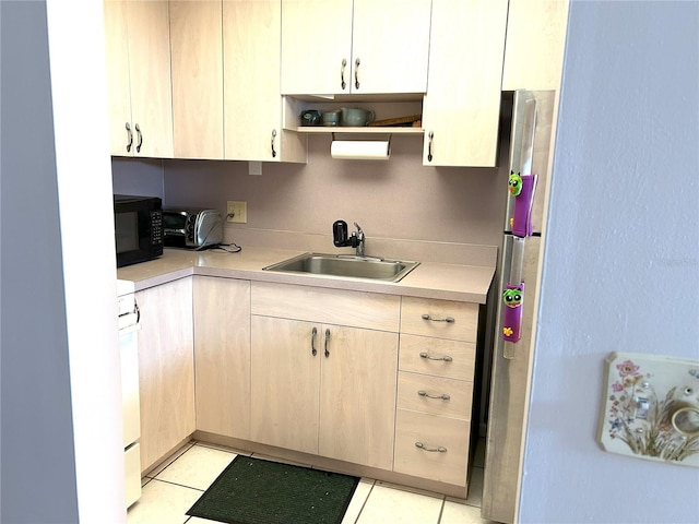 kitchen with stainless steel fridge, light brown cabinetry, sink, light tile patterned floors, and white stove