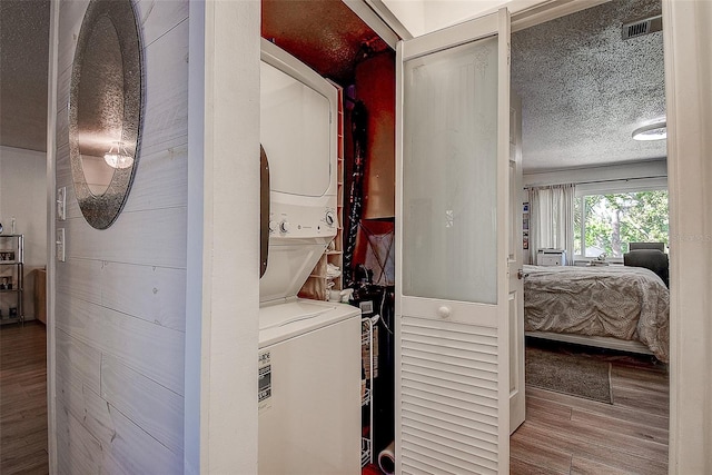 laundry area with a textured ceiling, hardwood / wood-style flooring, and stacked washer / drying machine