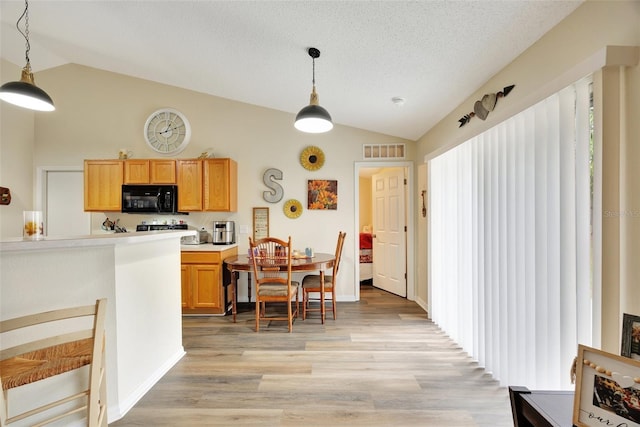 kitchen featuring a textured ceiling, light wood-type flooring, vaulted ceiling, and hanging light fixtures