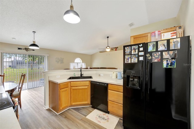 kitchen featuring kitchen peninsula, sink, black appliances, decorative light fixtures, and light hardwood / wood-style flooring