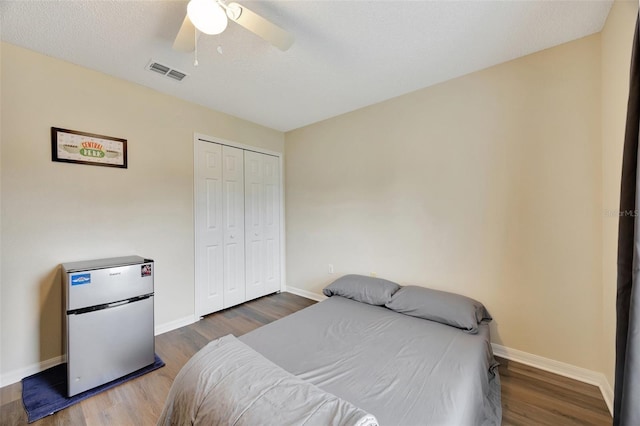 bedroom featuring dark hardwood / wood-style flooring, a textured ceiling, ceiling fan, stainless steel refrigerator, and a closet