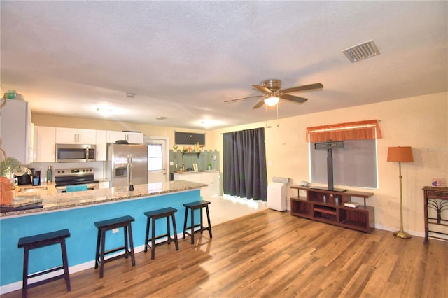 kitchen with wood-type flooring, kitchen peninsula, appliances with stainless steel finishes, light stone counters, and white cabinetry