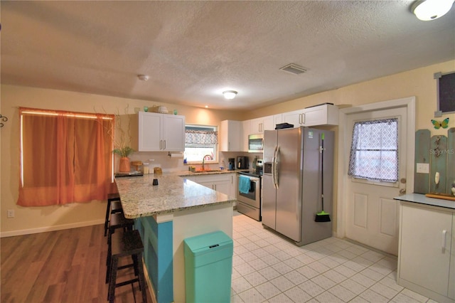 kitchen featuring a kitchen breakfast bar, sink, appliances with stainless steel finishes, white cabinetry, and kitchen peninsula