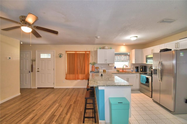 kitchen with ceiling fan, light wood-type flooring, appliances with stainless steel finishes, a kitchen bar, and white cabinetry