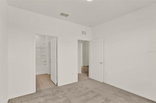 unfurnished bedroom featuring ensuite bath, light colored carpet, a walk in closet, and a closet